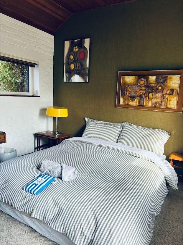 Bedroom 6 at Blue Waters with olive walls, whitewashed brick, a timber ceiling and a striped double bed
