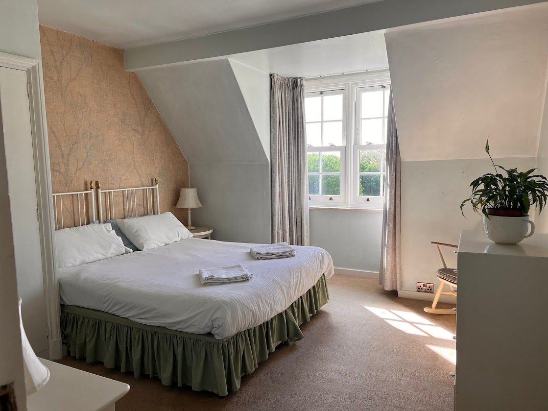 Bedroom 2 at Blue Waters with a white iron double bed, green bed valance and a window overlooking the garden