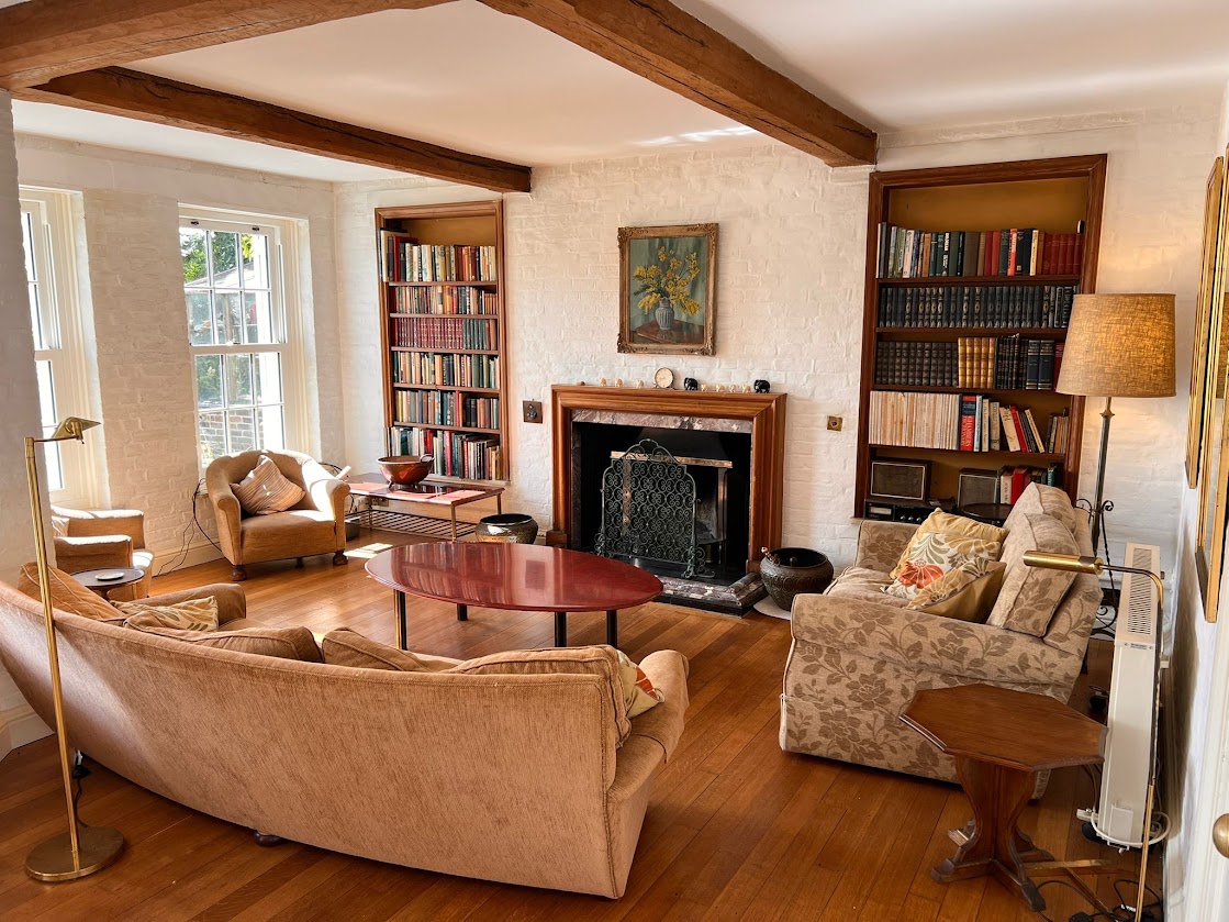 The sitting room at Blue Waters by day, with a marble fireplace, sash windows onto the garden, bookshelves and deep sofas