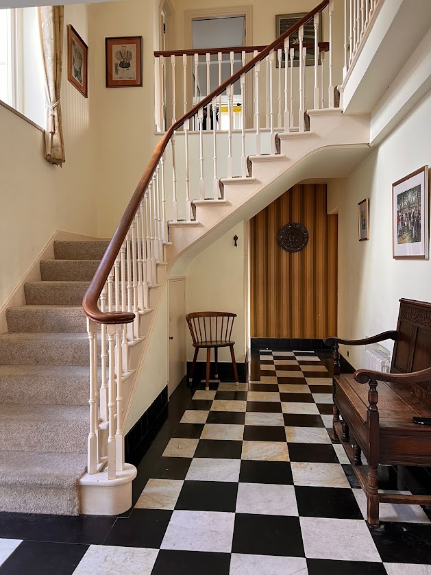 The hallway at Blue Waters with a black and white chequered marble floor, curved staircase and antique wooden bench