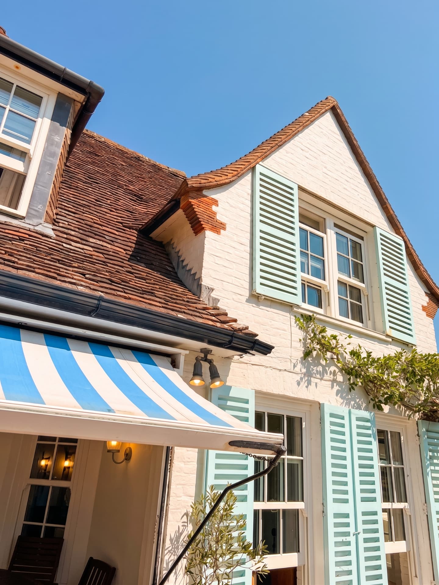 Blue Waters seen from the garden, with mint-green shutters and a striped blue-and-white awning over the terrace