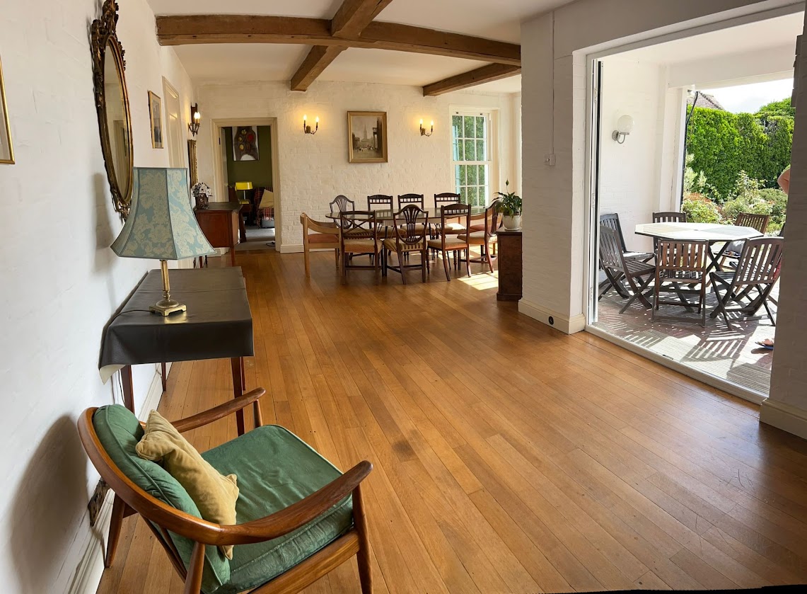 The dining room at Blue Waters from a wide angle, with the oval table and chairs, and doors open onto the terrace and garden